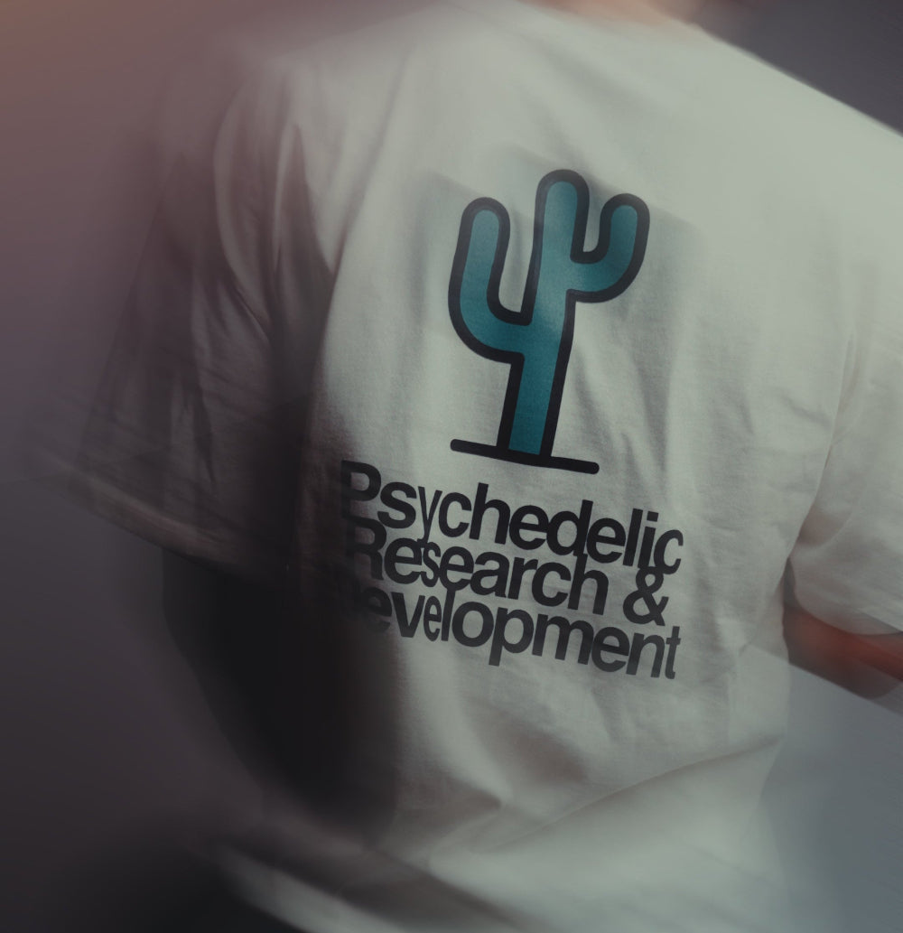White t-shirt with green cactus graphic and text 'Psychedelic Research & Development' on a plain background