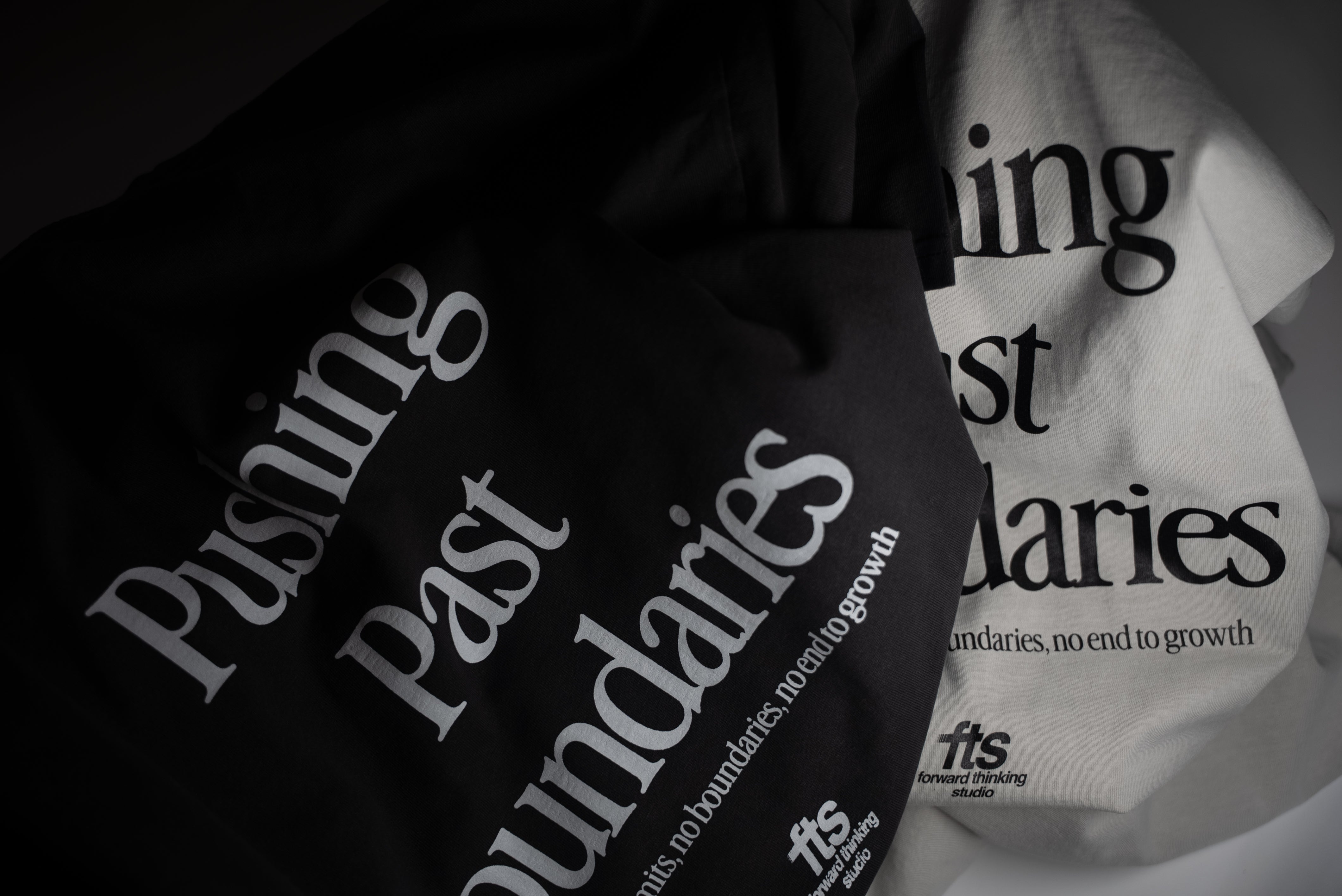 Black and white t-shirts with 'Pushing Past Boundaries' text on a dark background