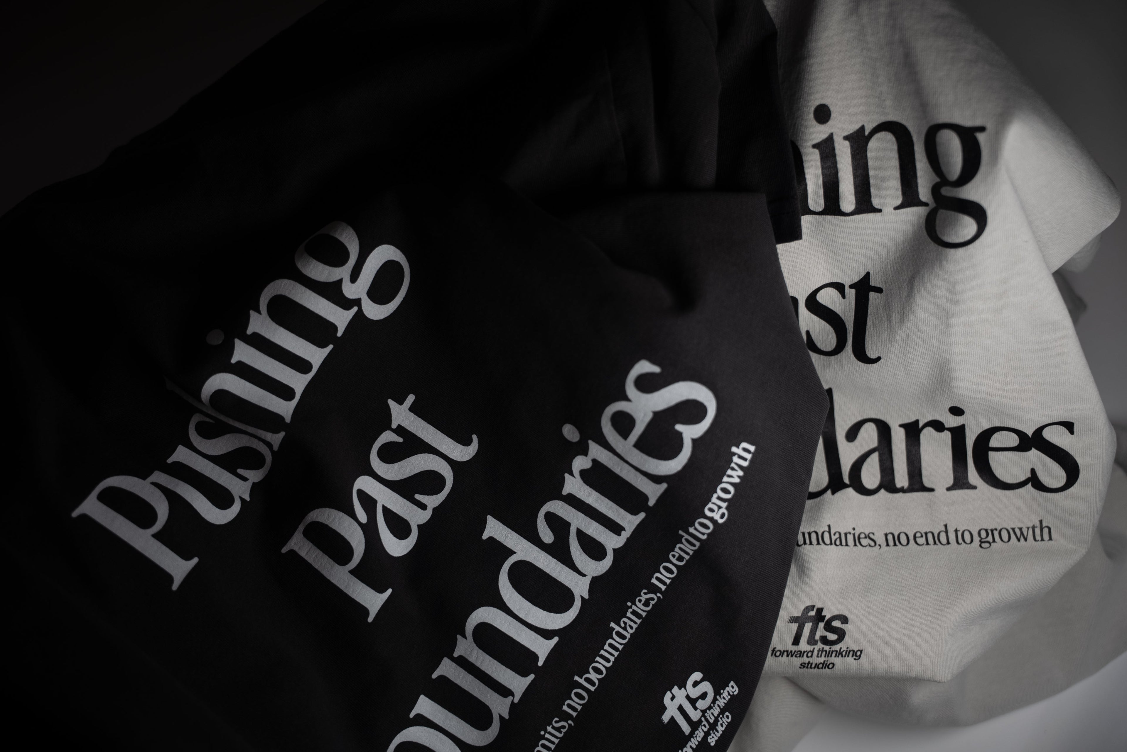 Black and white t-shirts with 'Pushing Past Boundaries' text on a dark background